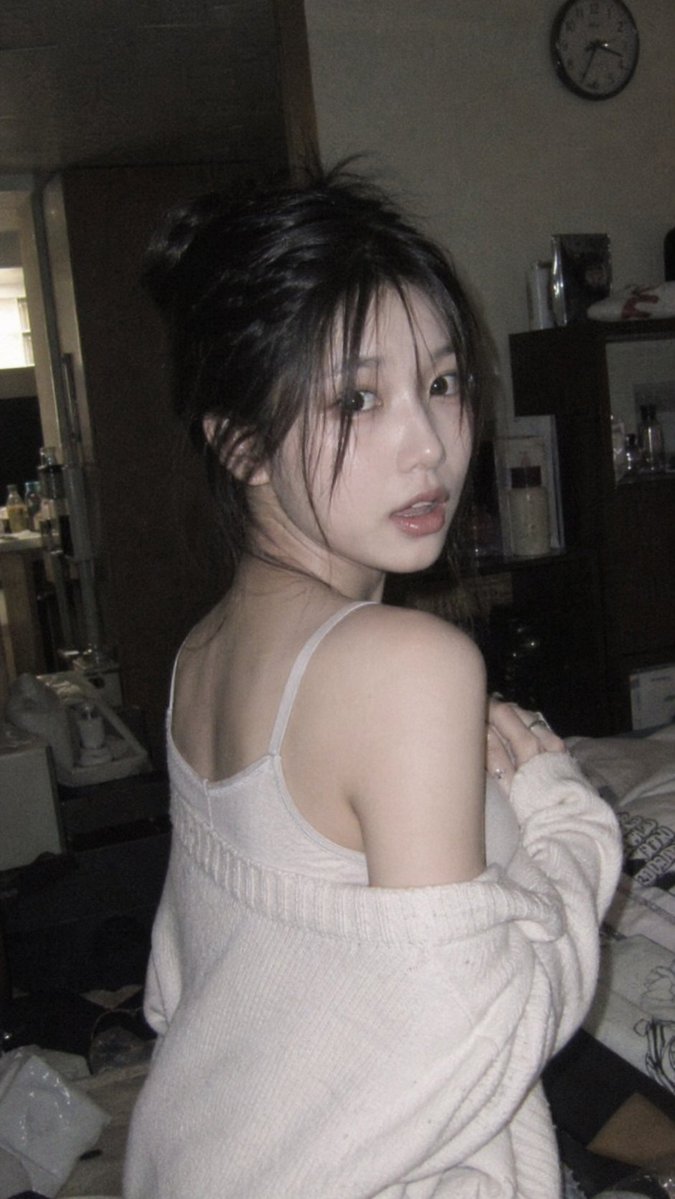 9:16 vertical candid portrait of a young Korean woman glancing back over her shoulder in a dimly...